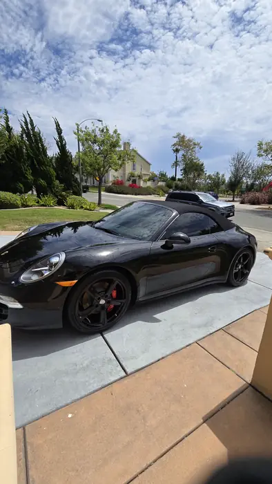 Black Porsche 911 Cabriolet in profile, the finish reflecting the sky after detailing