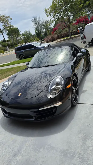 Tres cuartos delantero de un Porsche 911 Cabriolet negro después del detallado